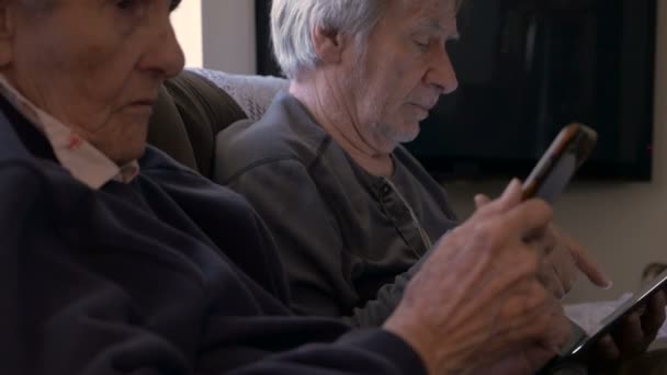 90 year old women and son look on their mobile devices, a cell phone and tablet - Séquence, vidéo