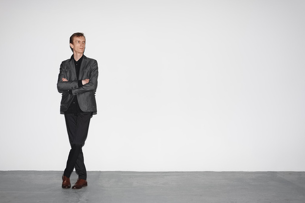 man in wool jacket standing near white concrete wall with crossed hands - Foto, afbeelding