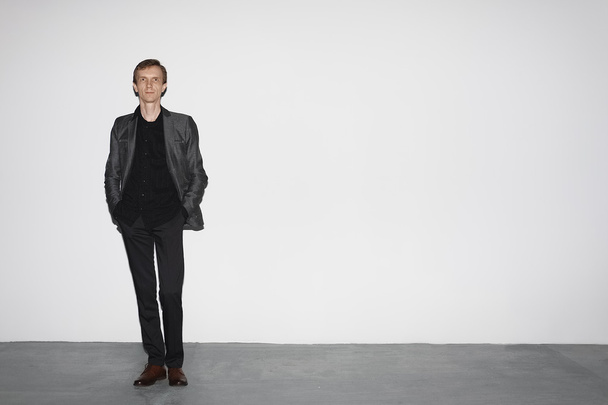 man in wool jacket standing near white concrete wall with hands in pocket - Photo, Image