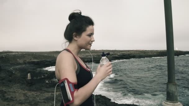 Woman drinking water while standing on rocks by sea - Materiał filmowy, wideo