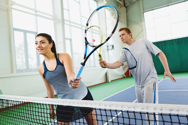 Nízký úhel pohledu rozhodný mladý muž a žena hrající tenis krytý - Fotografie, Obrázek