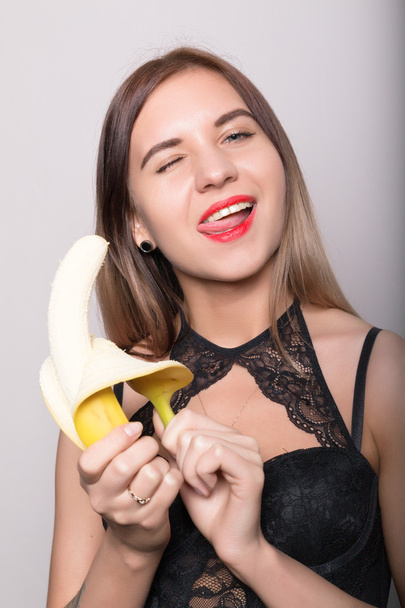 Young amazed woman in lacy lingerie holding a banana, she is going to eat a banana - Fotografie, Obrázek