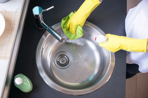 Hände in gelben Gummihandschuhen beim Waschen der Spüle - Foto, Bild