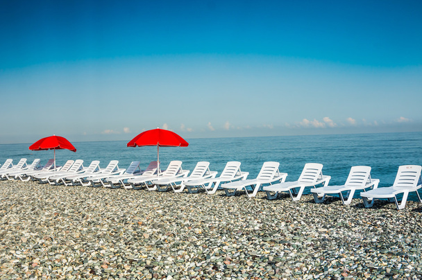 Лаунжі та червоні парасольки на пляжі
 - Фото, зображення