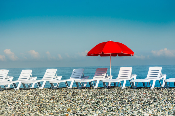 Ηλιοθεραπεία κρεβάτια πλαστικό και κόκκινη ομπρέλα στην παραλία - Φωτογραφία, εικόνα