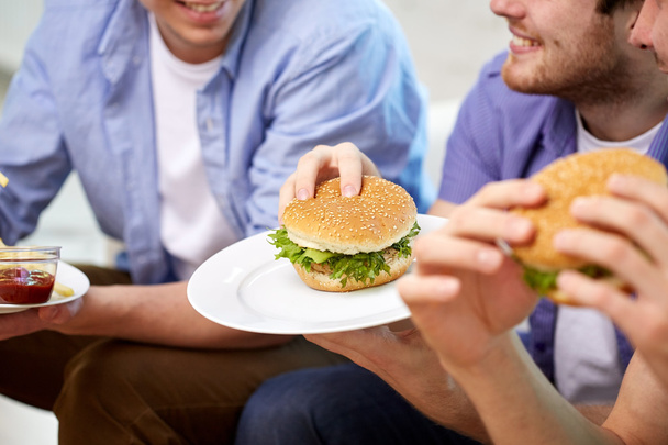 close up of friends eating hamburgers at home - Fotografie, Obrázek
