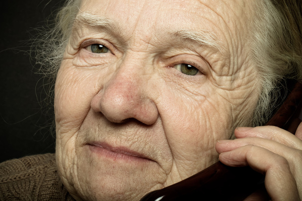 Portret van de oudere vrouw met telefoon op donkere achtergrond. Ton - Foto, afbeelding