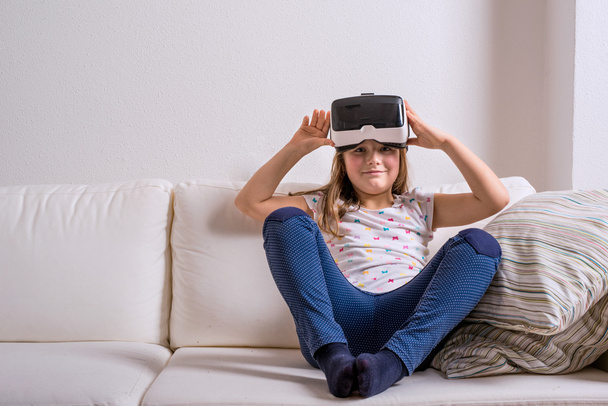 Girl wearing virtual reality goggles. Studio shot, white couch - Foto, Imagen