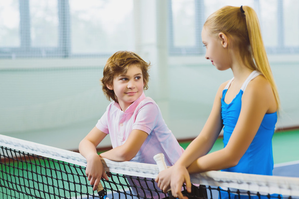 Cute children playing tennis and posing or resting in court indoor - Foto, Imagem