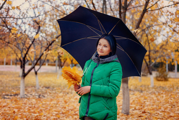 Χαριτωμένο νεαρή γυναίκα κρατώντας φύλλα και ομπρέλα - Φωτογραφία, εικόνα