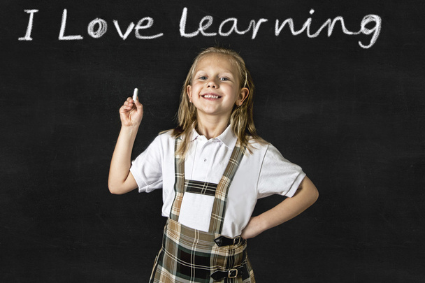 sweet junior blond schoolgirl smiling happy in front of school classroom blackboard - Photo, Image