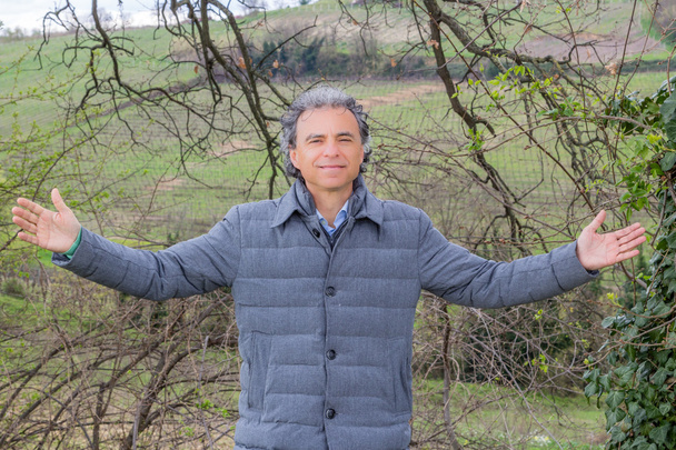 イタリアのエミリア・ロマーニャの田園地帯の耕地の前で腕を広げる中年男性 - 写真・画像