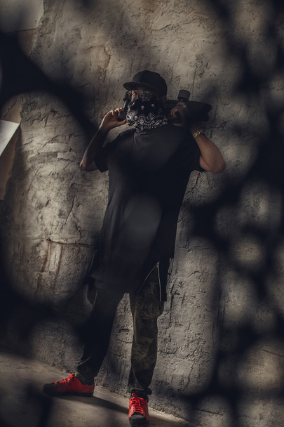 man in een masker houdt pistool en skateboard - Foto, afbeelding