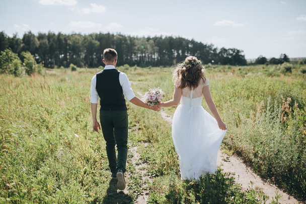 guy in a vest and a girl in a white wedding dress with a bouquet in the hands go on the field - Valokuva, kuva