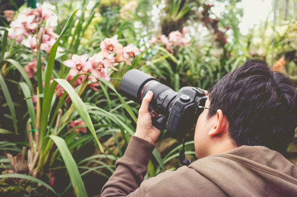 asiatischer Mann, der schöne Orchideenblumen in einem Orchideenhaus fotografiert. Jahrgangsstil. - Foto, Bild