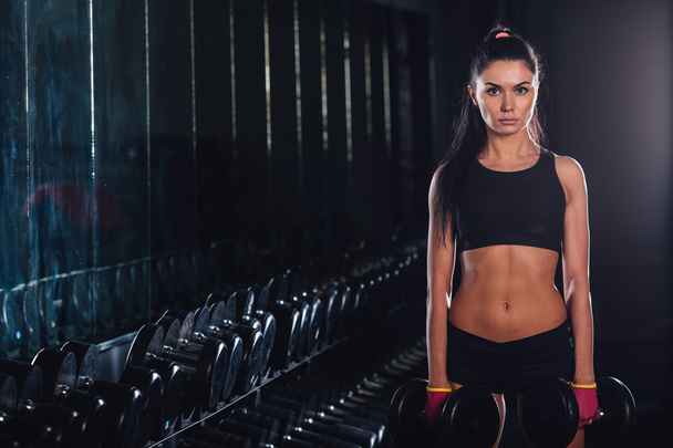 Young woman holding dumbbells in gym - Фото, изображение