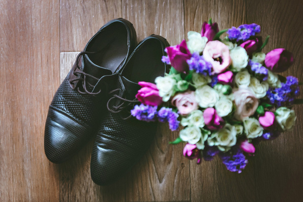 Purple, pink, white wedding bouquet of flowers. Mens black shoes on a wooden floor. - Photo, Image