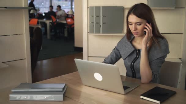 Femme d'affaires travaillant sur l'ordinateur portable et parlant par le téléphone portable dans le bureau séparé
. - Séquence, vidéo