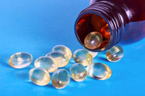 oil pills spilling out of prescription bottle on blue background - Foto, immagini