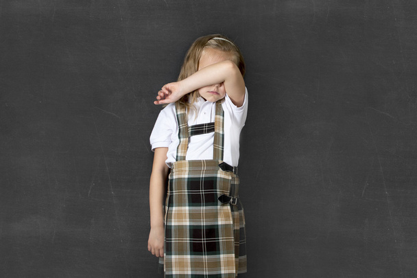 sweet junior schoolgirl with blonde hair crying sad and shy in front of school class blackboard  - Foto, afbeelding