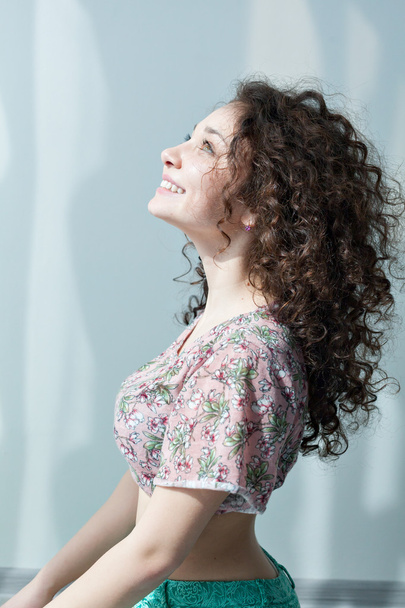 Young girl with curly hair smiling and enjoying life. Portrait in profile looking up. Tender feelings. Meditation. Practice yoga at home. Exercising in the morning in the bright sun room. - Photo, Image
