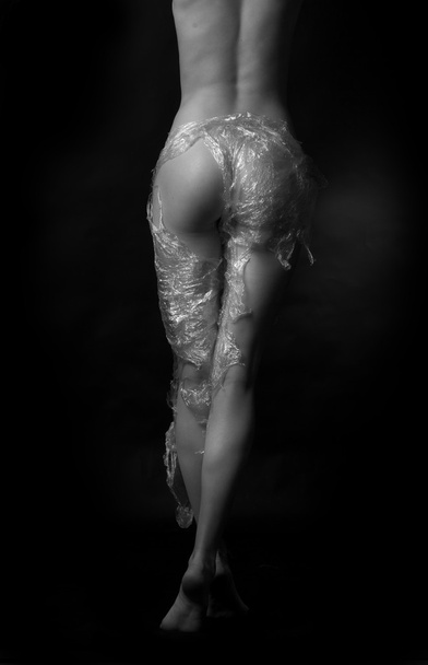 Naked girl, covered with plastic film on a dark background. - Foto, Imagem