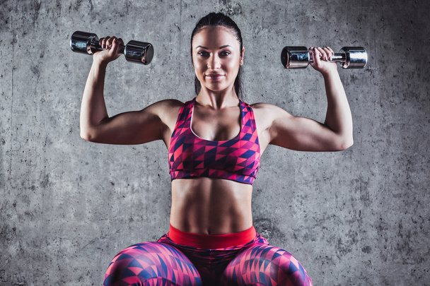 Beautiful muscular woman doing exercise with dumbbells on a gray background.Concrete wall in the background - Foto, immagini