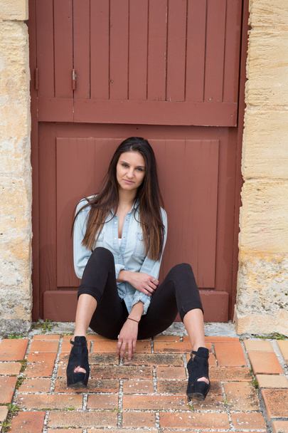 Habillée d'un blazer bleu, pantalon noir et chaussures à talons hauts, une adolescente brune est assise à l'extérieur
  - Photo, image