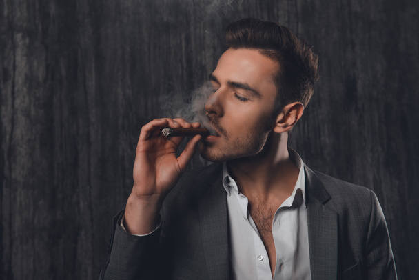 Portrait d'un jeune homme d'affaires en costume fumant un cigare
 - Photo, image