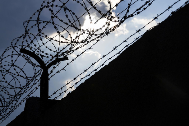Drámai felhők mögött szögesdrót kerítés a börtön falán  - Fotó, kép