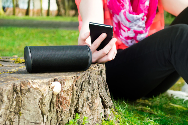 Woman is connecting her smartphone with wireless speaker while being outdoor. - Foto, Imagem