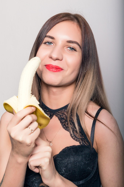 Young amazed woman in lacy lingerie holding a banana, she is going to eat a banana - Photo, Image