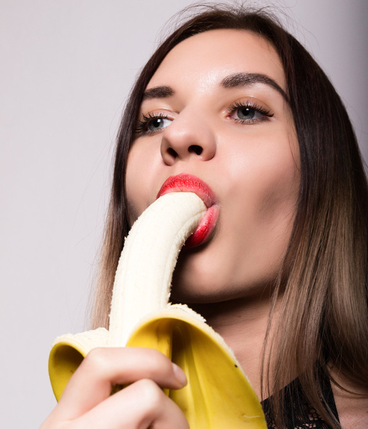 Young amazed woman in lacy lingerie holding a banana, she is going to eat a banana. she sucks a banana - Fotó, kép