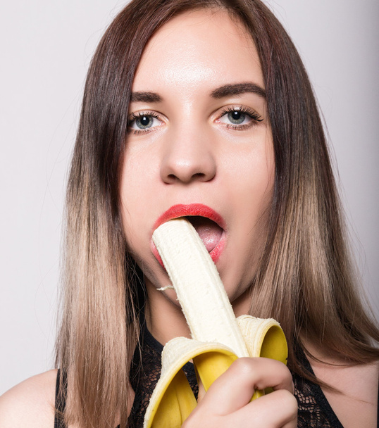 Young amazed woman in lacy lingerie holding a banana, she is going to eat a banana. she sucks a banana - Photo, Image