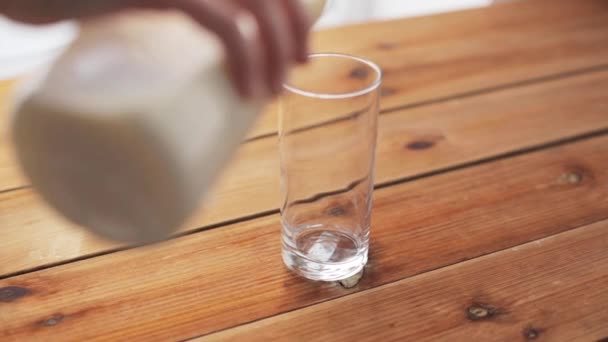 Hand gießt Milch in Glas auf Holztisch - Filmmaterial, Video