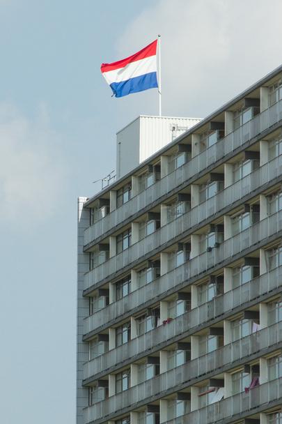 Bandera holandesa en la parte superior de un bloque de pisos contra el cielo azul
 - Foto, Imagen