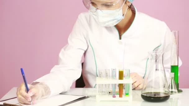Női kémikus összehasonlítása vegyszerekkel kémcsövek. védőszemüveg - Felvétel, videó