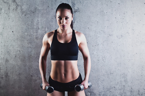 Beautiful muscular woman doing exercise with dumbbells on a gray background. - 写真・画像