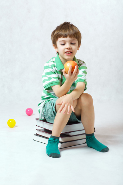 Un garçon mangeant une pomme assis sur un tas de livres
 - Photo, image