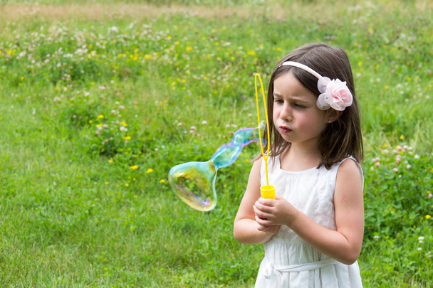 Petite fille en robe blanche soufflant des bulles au parc
 - Photo, image