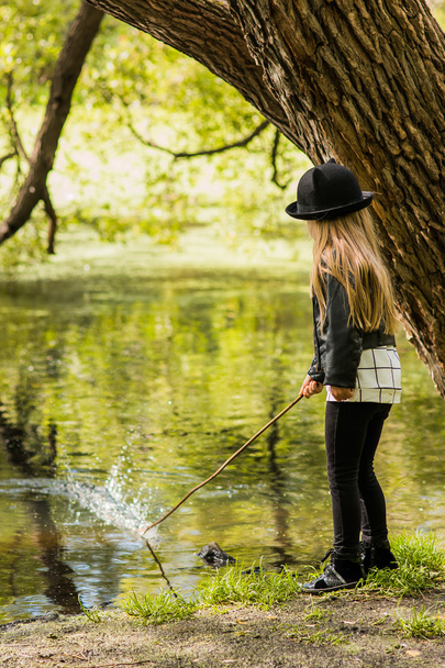Girl in a hat walking in the park summer day and stick fishing in the river - Foto, Imagen