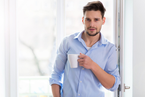 Man drinking cup of coffee near window - Фото, изображение