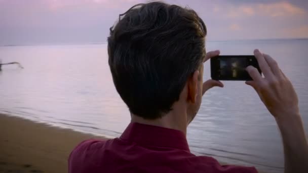 Hand-het gehouden shot van een slimme telefoon van middelste leeftijd man fotograferen op het strand - Video
