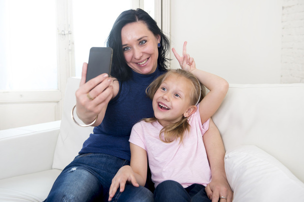νεαρή γυναίκα ευτυχισμένη με την μικρή χαριτωμένο Ξανθιά κόρη λαμβάνοντας αυτοπορτρέτα φωτογραφία με το κινητό τηλέφωνο - Φωτογραφία, εικόνα