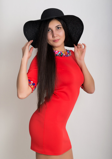 Beautiful asian young brunette in a little red dress and big black hat, standing and posing - Photo, image