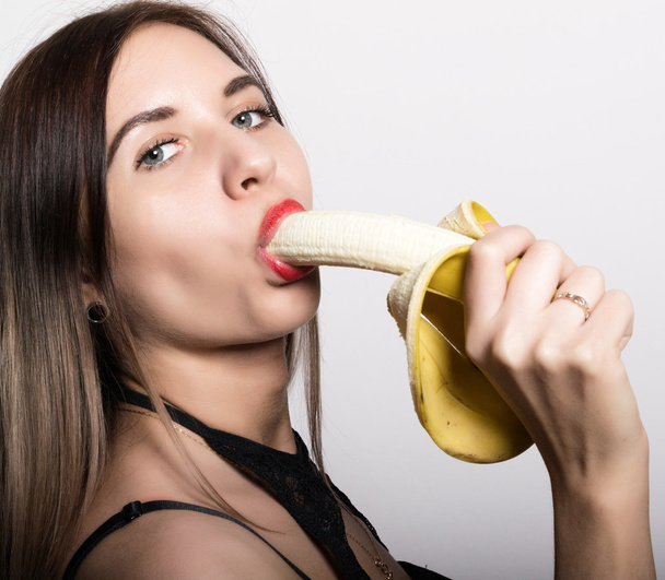 Young amazed woman in lacy lingerie holding a banana, she is going to eat a banana. she sucks a banana - Zdjęcie, obraz