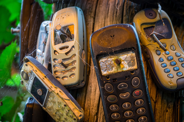 Old mobile phones are nailed to a trunk. The severely damaged mobile phones transfer the message that phones are to be turned off here. - Zdjęcie, obraz