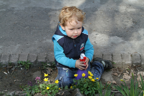 White kid with a spray helps parents take care of the flowers an - Photo, Image