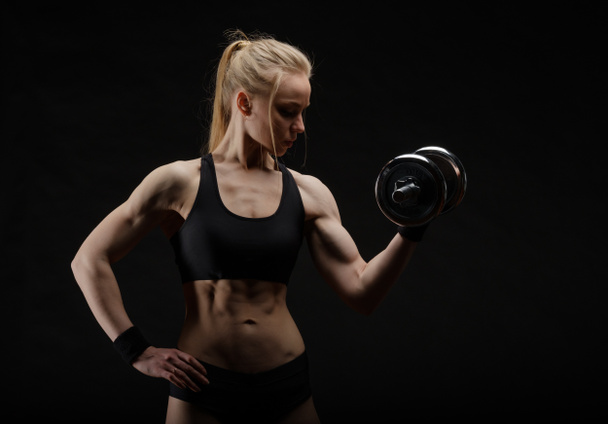 Young slim strong muscular woman posing in studio with dumbbell - Photo, Image