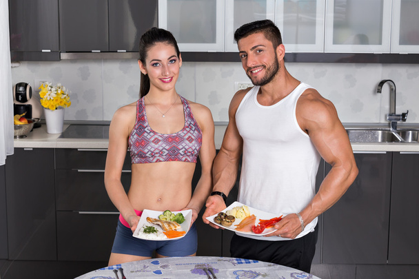 fit couple in the kitchen, holding plates of food - Photo, Image